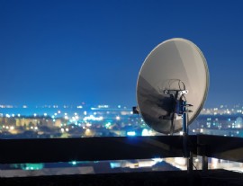 Satellitenantenne auf einem Dach mit einer Stadt im Hintergrund bei Nacht